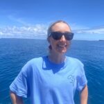 A profile picture of Claire Collins standing in front of a marine seascape taken in Chagos.