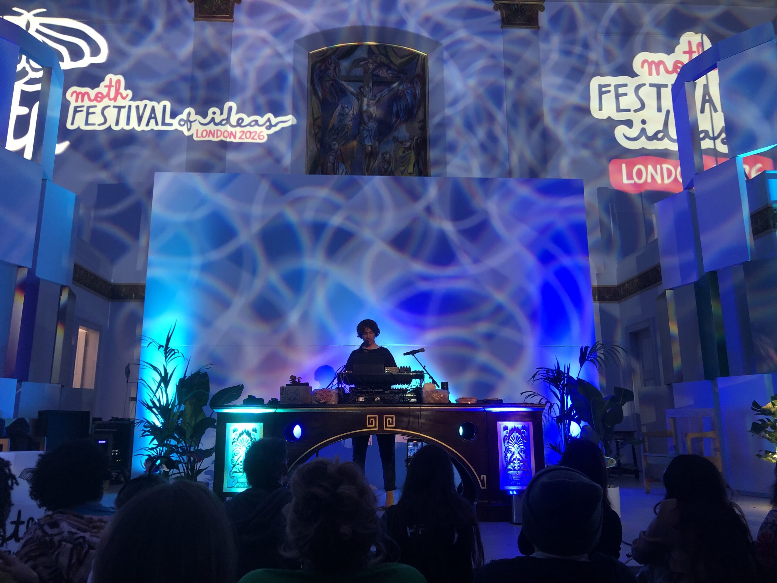 A sihouette of Cosmo Sheldrake DJ-ing with electric blue shining lights in the background