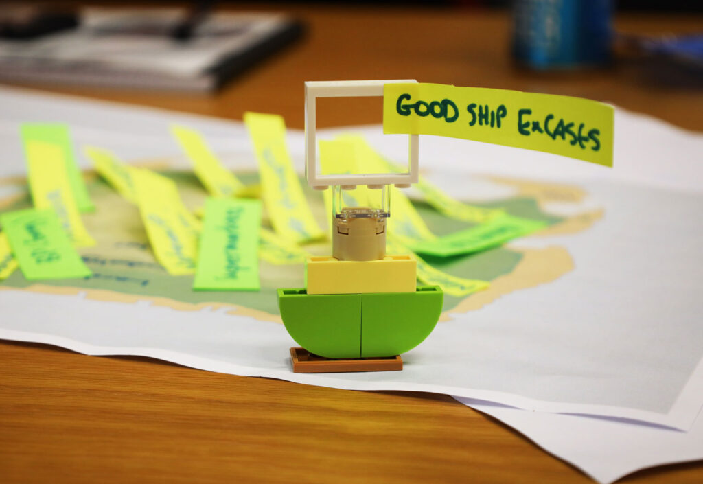A photo of a small lego boat with 'Good ship ExCASES' written on a paper sail